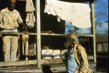 A farmer stands on his porch and talks to a bearded scientist (Robert Horwich).